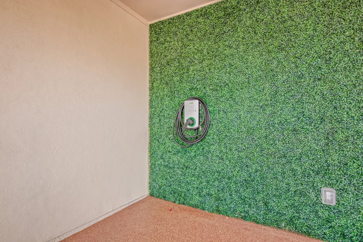 A contemporary interior scene featuring a green textured wall with a visible electric vehicle charging station. The area is clean, modern, and designed with sustainability in mind, signaling advanced practical amenities for guests.