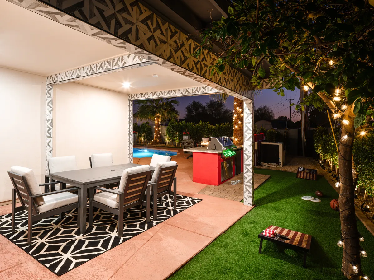 A stylish outdoor dining table sits beside a grill and a shimmering pool, illuminated by delicate string lights overhead. The setup is perfect for alfresco meals and casual gatherings that extend into the evening.