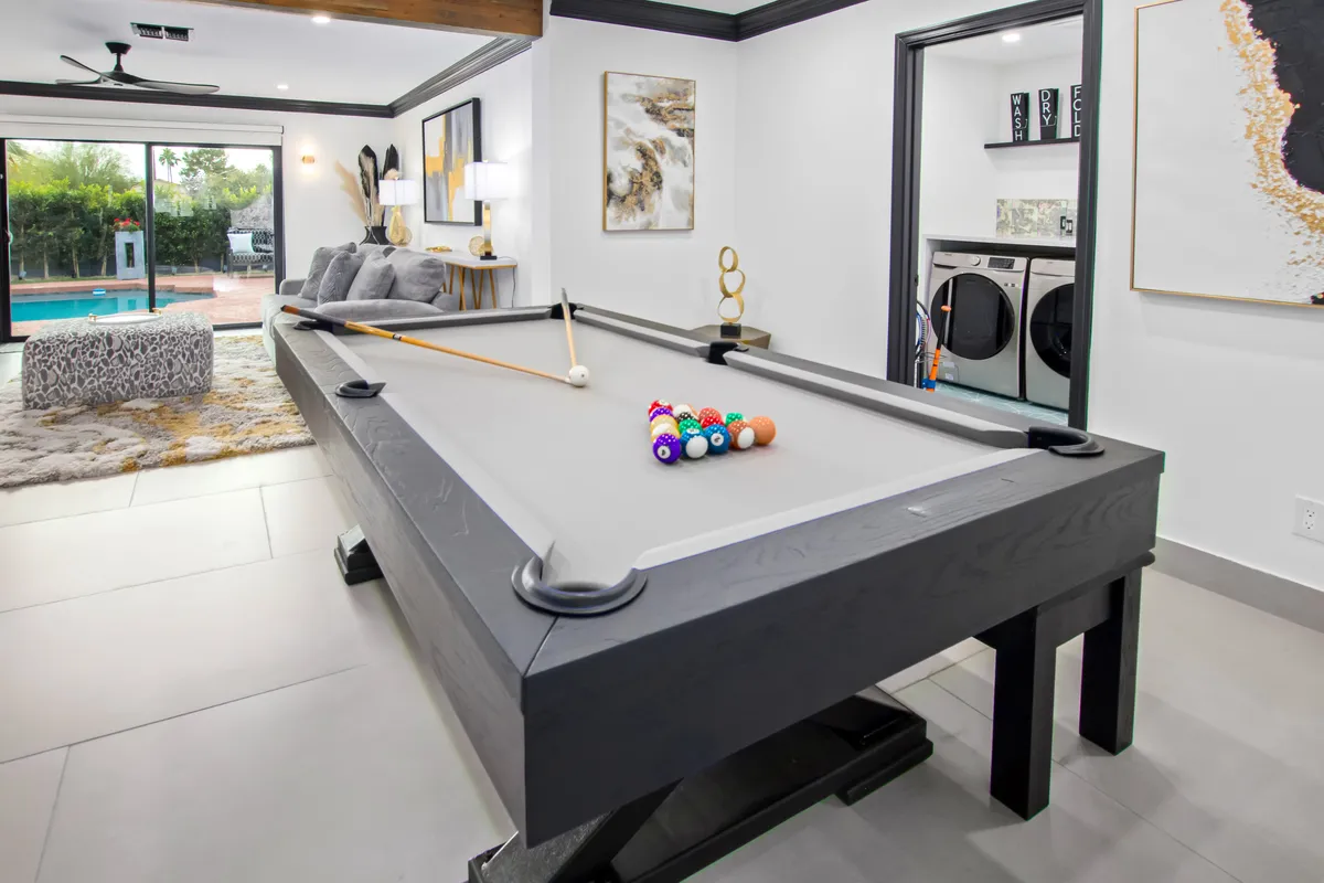 A playful, open lounge with a pool table that doubles as a dining area. Nearby, a sofa and modern artwork create a relaxed, fun atmosphere ideally suited for both casual hangouts and friendly competitions. The laundry area can be seen in the background, subtly indicating the home's functionality.