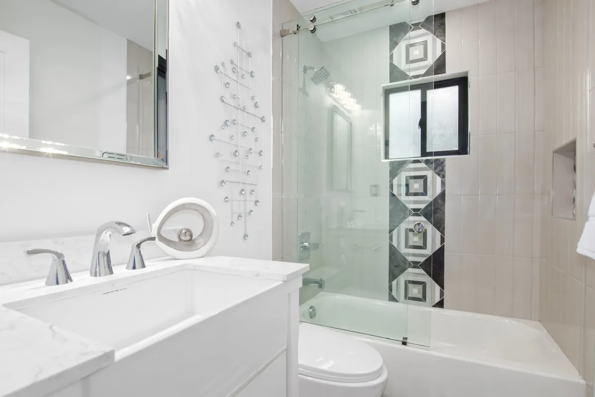 A bright, spa-inspired bathroom with a white double sink vanity, geometric tiled wall, and a glass shower enclosure. The mood is refreshing and inviting, echoing a luxurious retreat experience.