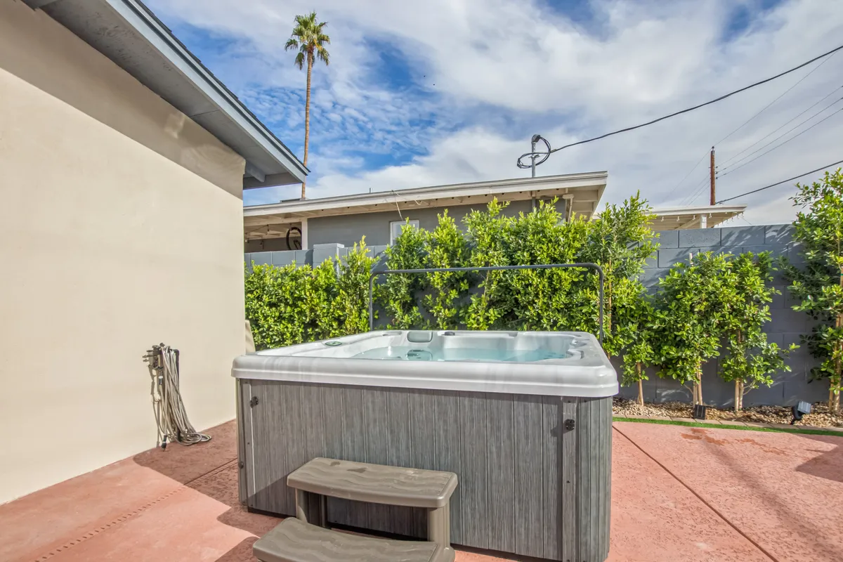A tranquil hot tub is featured amidst lush greenery and an inviting patio area. The scene suggests both daytime relaxation and nighttime stargazing, with comfortable seating for small gatherings.