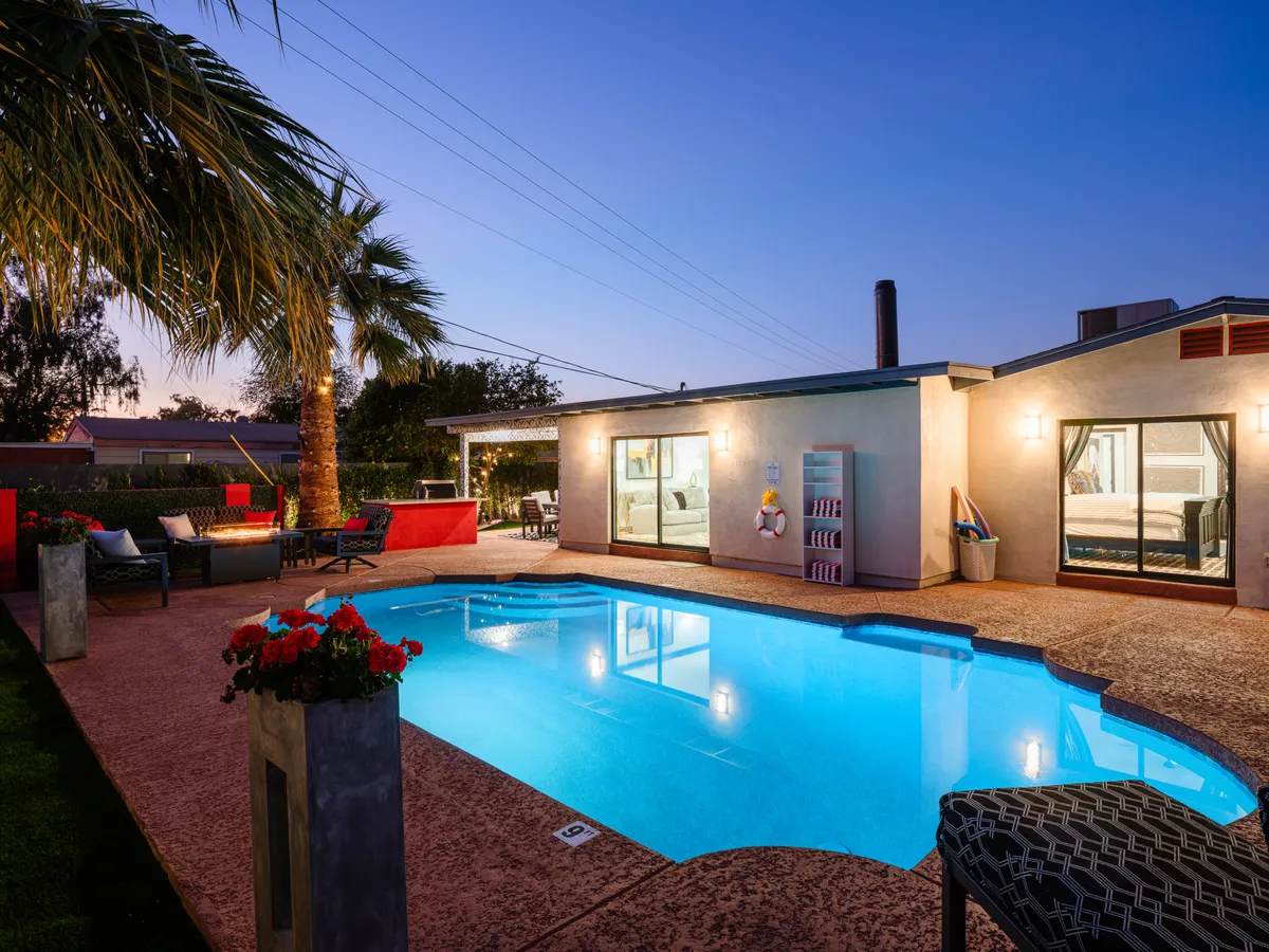 A private fenced backyard with a sparkling swimming pool, palm trees, and a comfortable outdoor seating area. The space is tranquil and perfect for unwinding after a day out, while providing ample room for pets to relax safely.